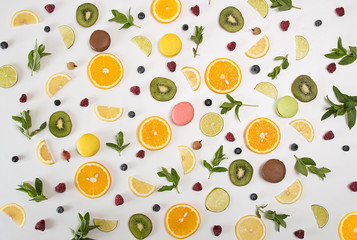 Flat lay still life with macarons, berries, mint, lemon, orange fruit, lime, kiwi