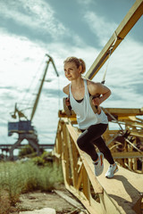 Cheerful woman exercising with suspension trainer outdoor. Trx training against the background of metal parts.