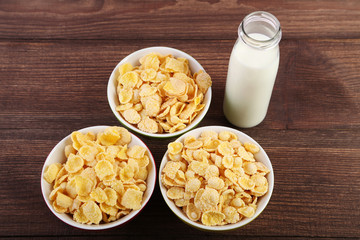 Cornflakes in bowls and bottle of milk on wooden table