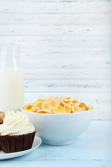Cornflakes, bottle of milk and cupcake on wooden table