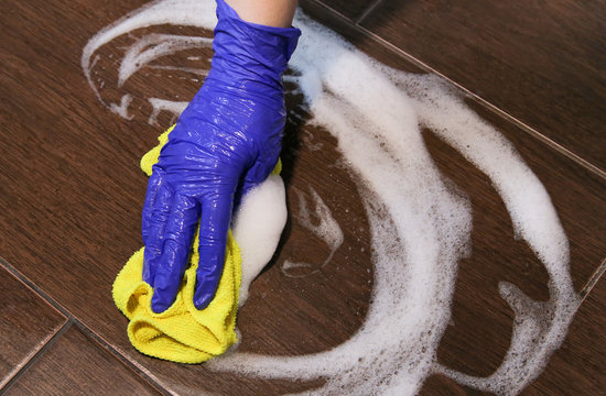 Closeup on woman's hands in blue protective rubber gloves cleaning kitchen and tiles