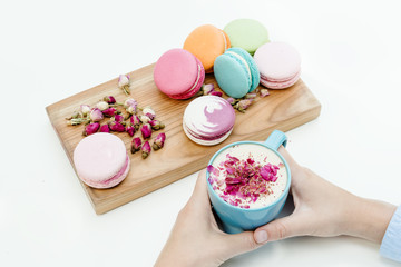 Fototapeta na wymiar View on woman hands holding a blue cappuccino cup and beauty french macarons