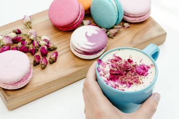 Obraz na płótnie Canvas Beauty french macarons on wood desk and hand holding blue cup of cappuccino on white background table