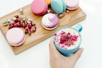 Obraz na płótnie Canvas Woman hand hold cappuccino cup with roses petals. Beauty french macarons on wood desk and white background