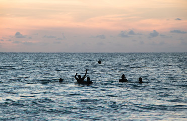 Naklejka premium Teenagers Playing Ball in Ocean at Dusk 