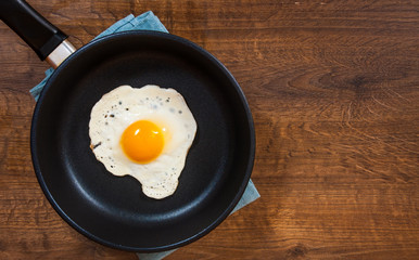 Fried egg in a frying pan on the brown wooden table background. with copy space. top view.