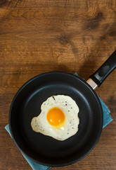Fried egg in a frying pan on the brown wooden table background. with copy space. top view.
