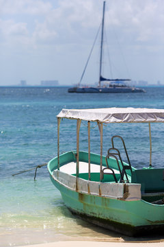 Old and rusty fishing boat on the shore. Turquoise water. Sailboat on the background out of focus.