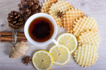 Cup of tea with Christmas decor, waffles and cinnamon, lemon, ginger, pinecone, badian
