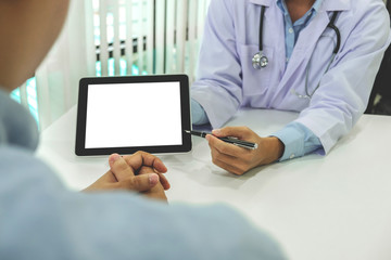 Doctor consulting patient and recommend treatment methods and how to rehabilitate the body, presenting results on tablet computer in hospital office
