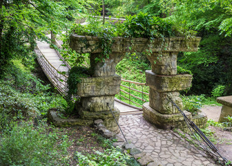 Wooden hanging bridge in the garden. Entrance to the bridge is decorated with stone arch support