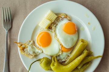 Morning Breakfast. White Plate with fried eggs, pieces of cheese and green baked pepper. The dish is on the table, which is covered with a tablecloth. A fork lies next to it. 
