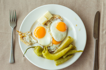 Breakfast. Plate with fried eggs, pieces of cheese and green baked pepper. The dish is on the table, which is covered with a tablecloth. A fork lies next to it. 