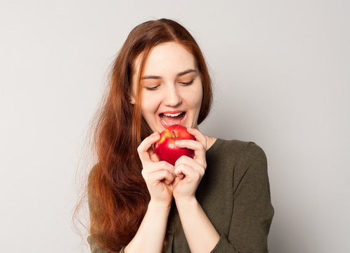 A young pretty girl bites a bright red juicy ripe apple full of vitamins and fiber. Healthy vegetarian food, diet for weight loss.