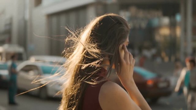 Sunset shot of young brunette girl walking down the street and have pleasant talk by smartphone,120FPS slowmotion