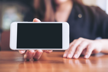 Mockup image of a woman holding and showing white horizontal mobile phone with blank black screen...