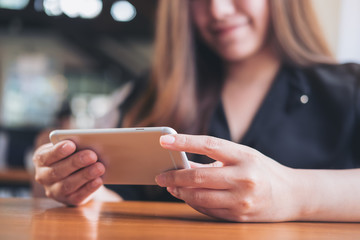 A beautiful Asian woman with smiley face holding and using horizontal smart phone to watching tv and playing games in modern cafe