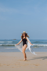 Girl in a black swimsuit and hat walking and whirls on the beach 