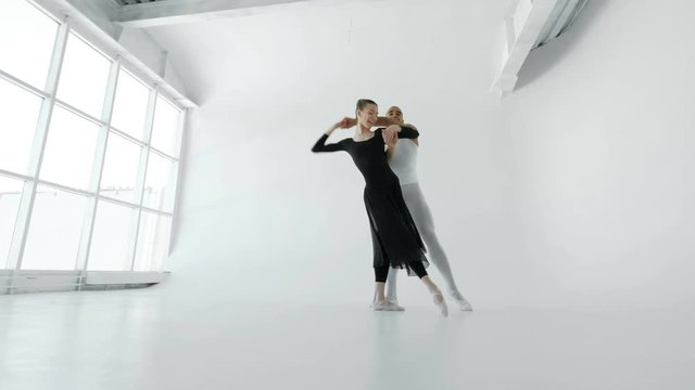 Young and attractive dancers in white and black gracefully dance in a white ballet hall with a large window shot from below 4k.