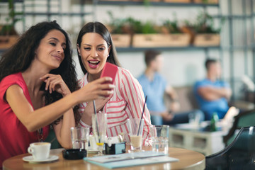 Two friends enjoying coffee together in a coffee shop as they sit at a table chatting