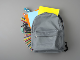 Top view of a backpack and school supplies on grey wooden table