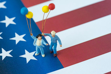 miniature happy american family holding balloons standing on United State national flag as Independence day celebration