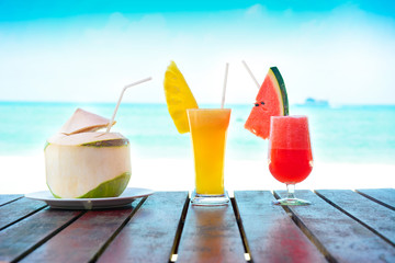 Colorful fruit smoothie drinks and coconut juice on the table in beach background