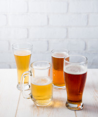 Beer glasses with various beer on wood table against white brick wall