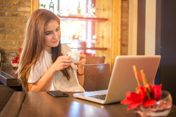 Teenage girl having coffee cup and learning on laptop in a cafe.