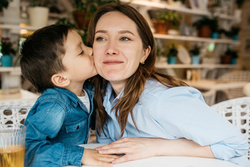 A small boy 4-5 years old kisses his mother on the cheek. In a cozy bright room