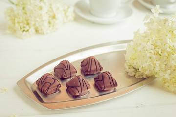 Chocolate candies on an iron plate on a white background with flowers