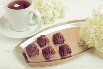 Chocolate sweets with a cup of coffee or tea on a white wooden table.