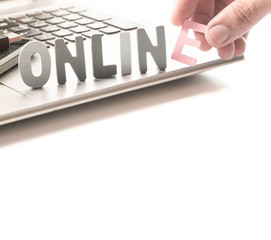 ONLINE word made from colored wooden letters on laptop with smartphone,human's finger at E letter.