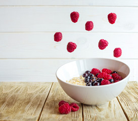 Plate of oatmeal with blueberries and raspberries on white background. Vegetarian breakfast. Flying fruit