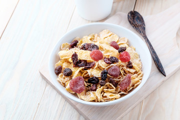 cornflakes and dry berry fruits in a white bowl on a wooden background.