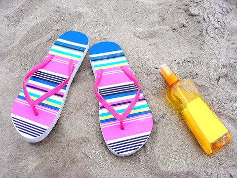 Colorful flip-flops and sun-care milk on a sandy beach