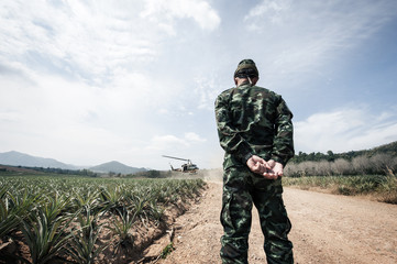 A soldier is waiting for chopper taxiing on a field, Thai Army Helicopter is landing on the open field operation site.