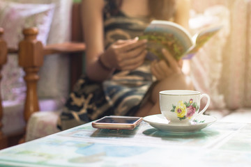 Beautiful young asian woman sitting on chair relaxing coffee time with book and smartphone at home