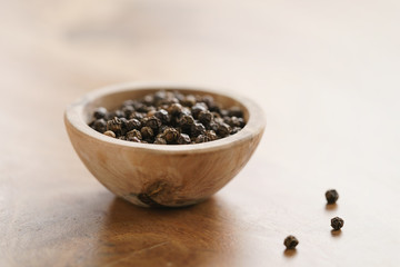 Fototapeta na wymiar black dry pepper in wooden bowl on table