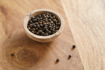 black dry pepper in wooden bowl on table