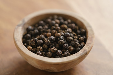 black dry pepper in wooden bowl on table