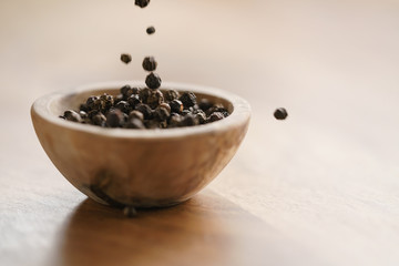 Fototapeta na wymiar black dry pepper falling in wooden bowl on table