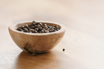 black dry pepper in wooden bowl on table