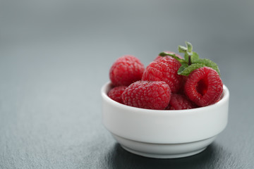 fresh raspberries with mint leaves in white bowl on slate board