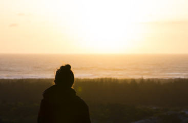 Silhouette of young woman looking out at sunset on pacific coast of Oregon