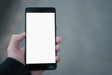 man hand holding smartphone with white screen outdoors with asphalt blurred background