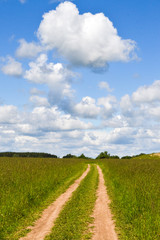 Country road through the field. Sky with clouds