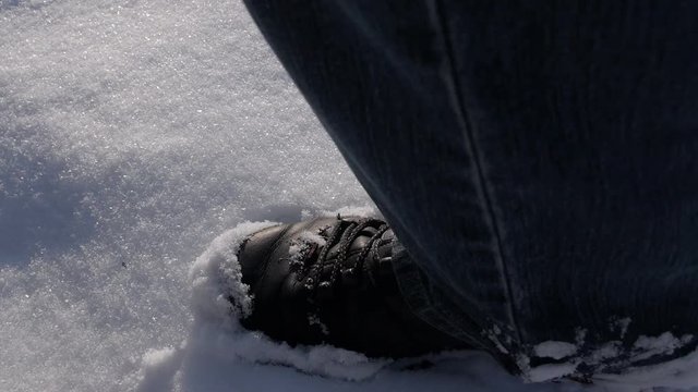 Male legs in black boots walking in white snow. A trail of shoes left in the snow
