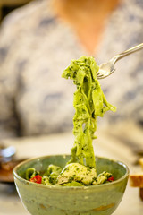 Green pasta with herbs on a fork.