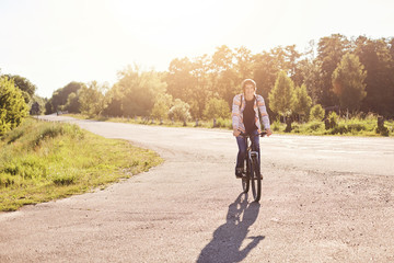 People, sports and healthy active lifestyle concept. Smiling hipster schoolboy with trendy hairdo riding bicycle outdoors. Young cyclist having vacations travelling with bicycle admiring nature